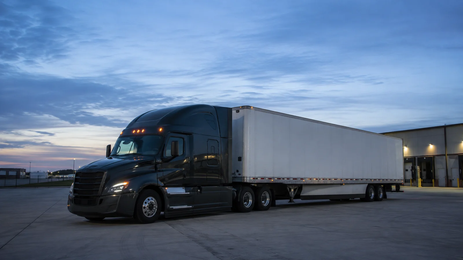 Unbranded tractor and trailer beside a desert-edge industrial facility at blue hour